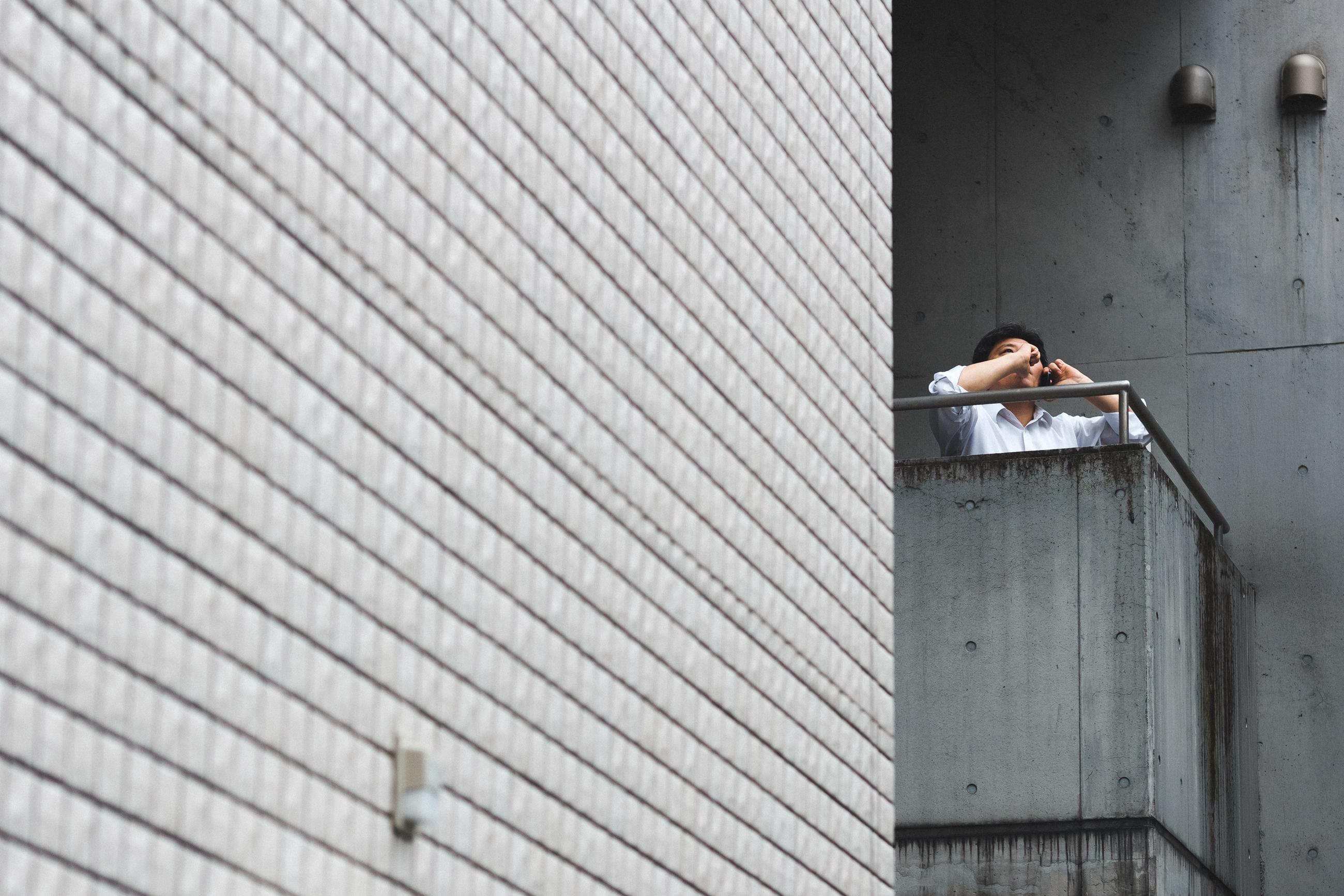 A guy on the phone staring longingly from a balcony
